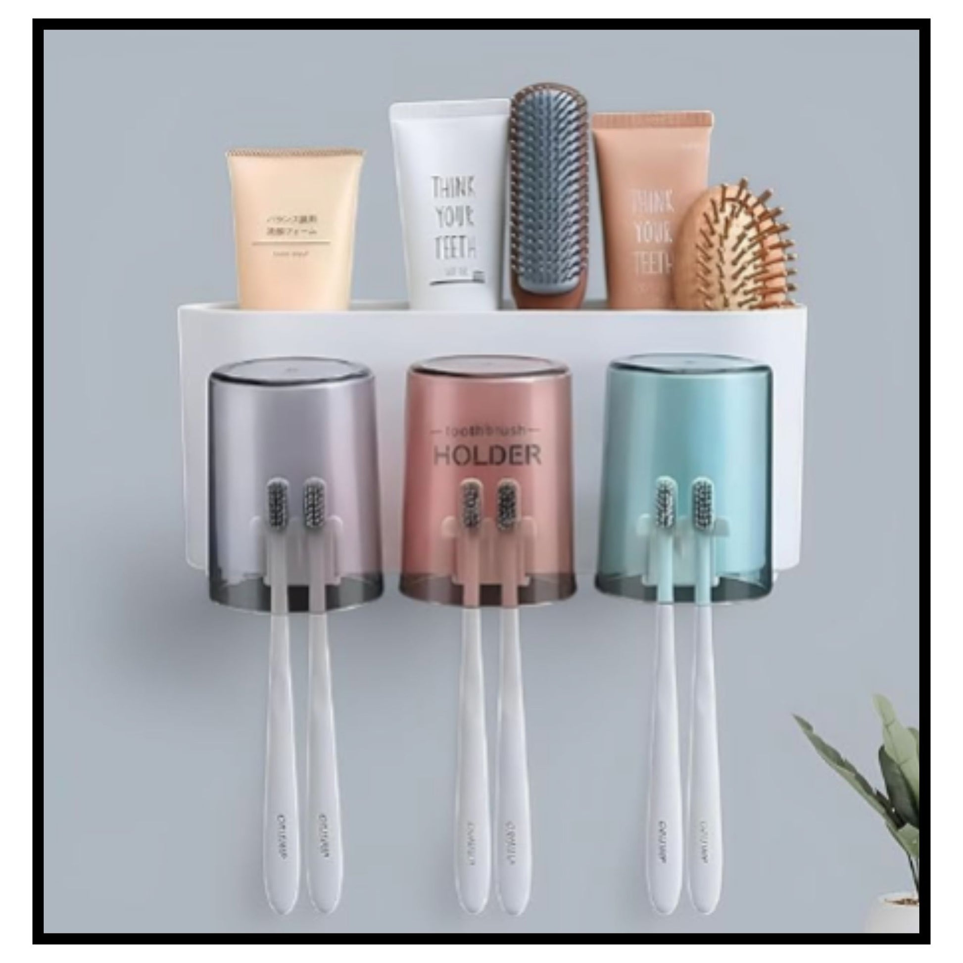 Wall-mounted white toothbrush holder set with three translucent cups in gray pink and green holding toothbrushes and top shelf with toothpaste